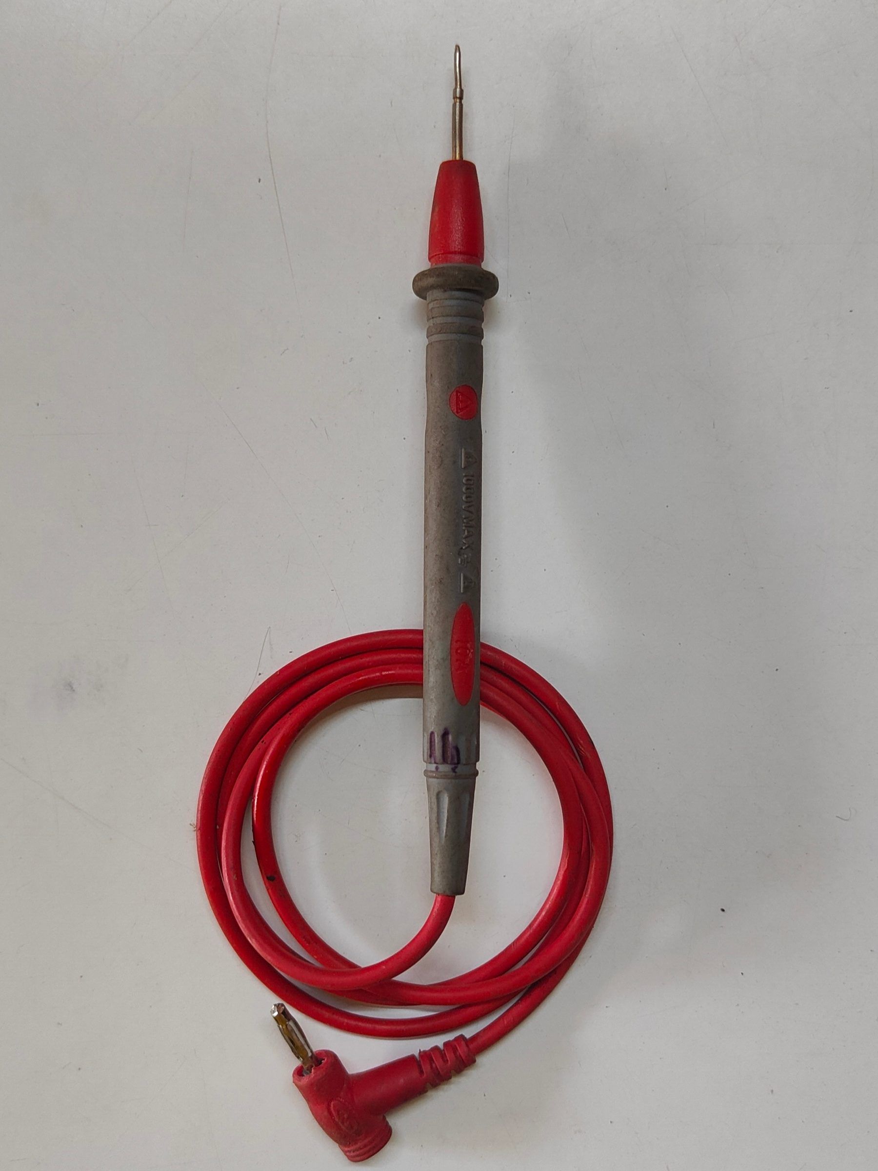 A multimeter test probe with a red tip and a coiled red lead on a pale gray surface