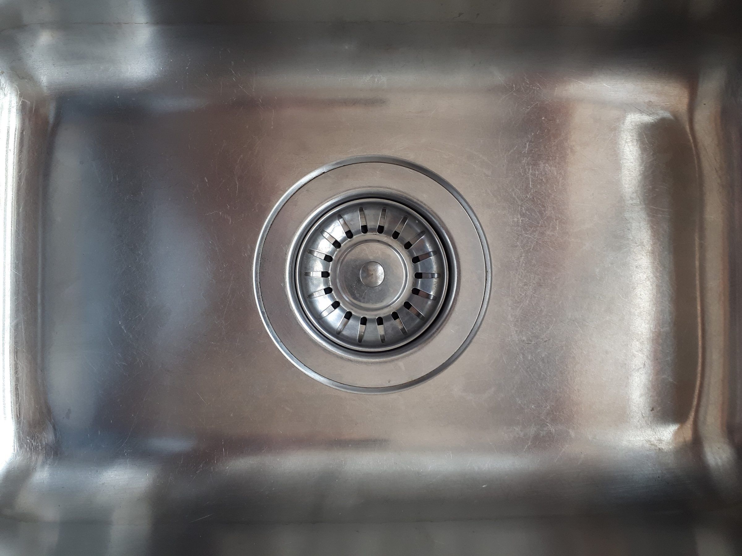 Top-down view of a brushed stainless sink bowl with a slotted strainer in the drain
