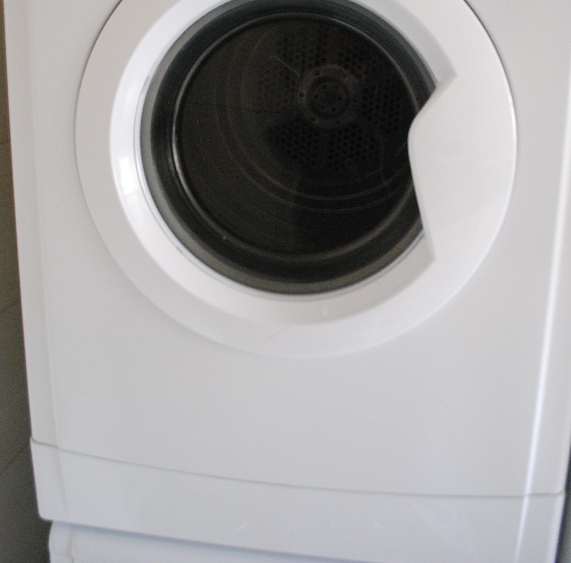Front of a white dryer with its round door and the dark drum inside
